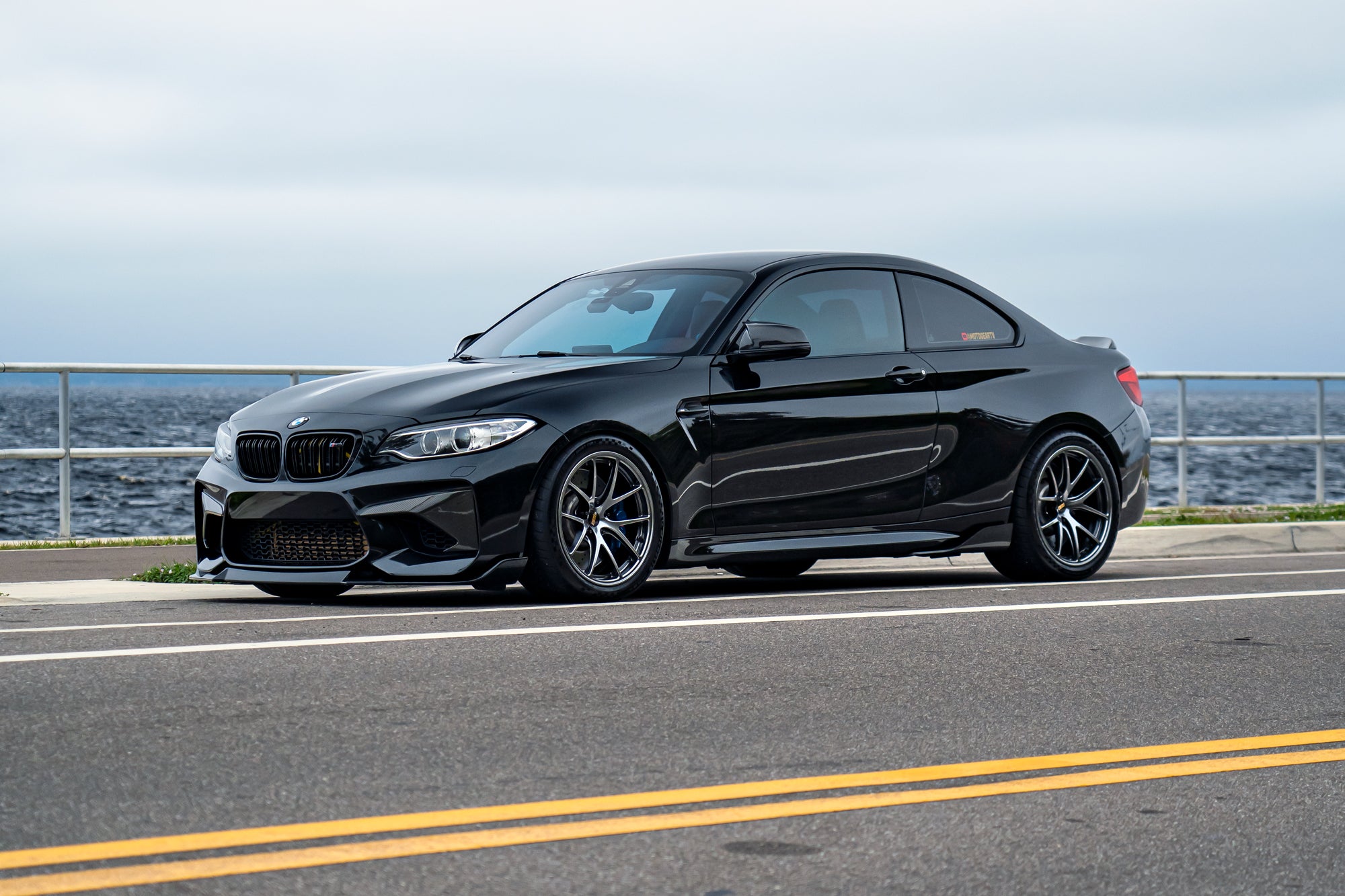 Modified BMW F87 M2 parked beside lake.